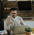happy-entrepreneur-drinking-coffee-during-conference-call-laptop-home
