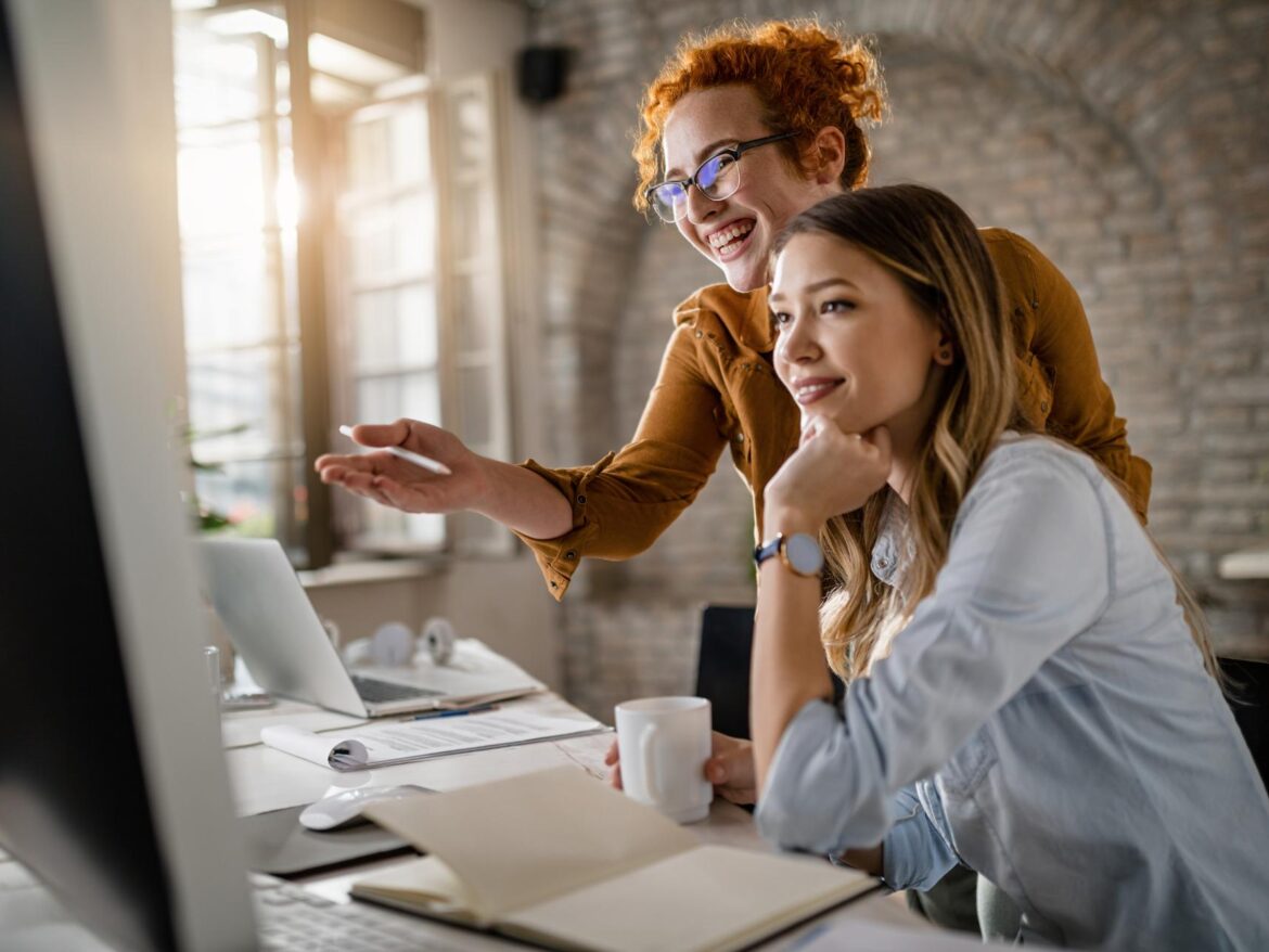 happy-female-entrepreneurs-reading-email-computer-while-working-together-office-focus-is-redhead-woman